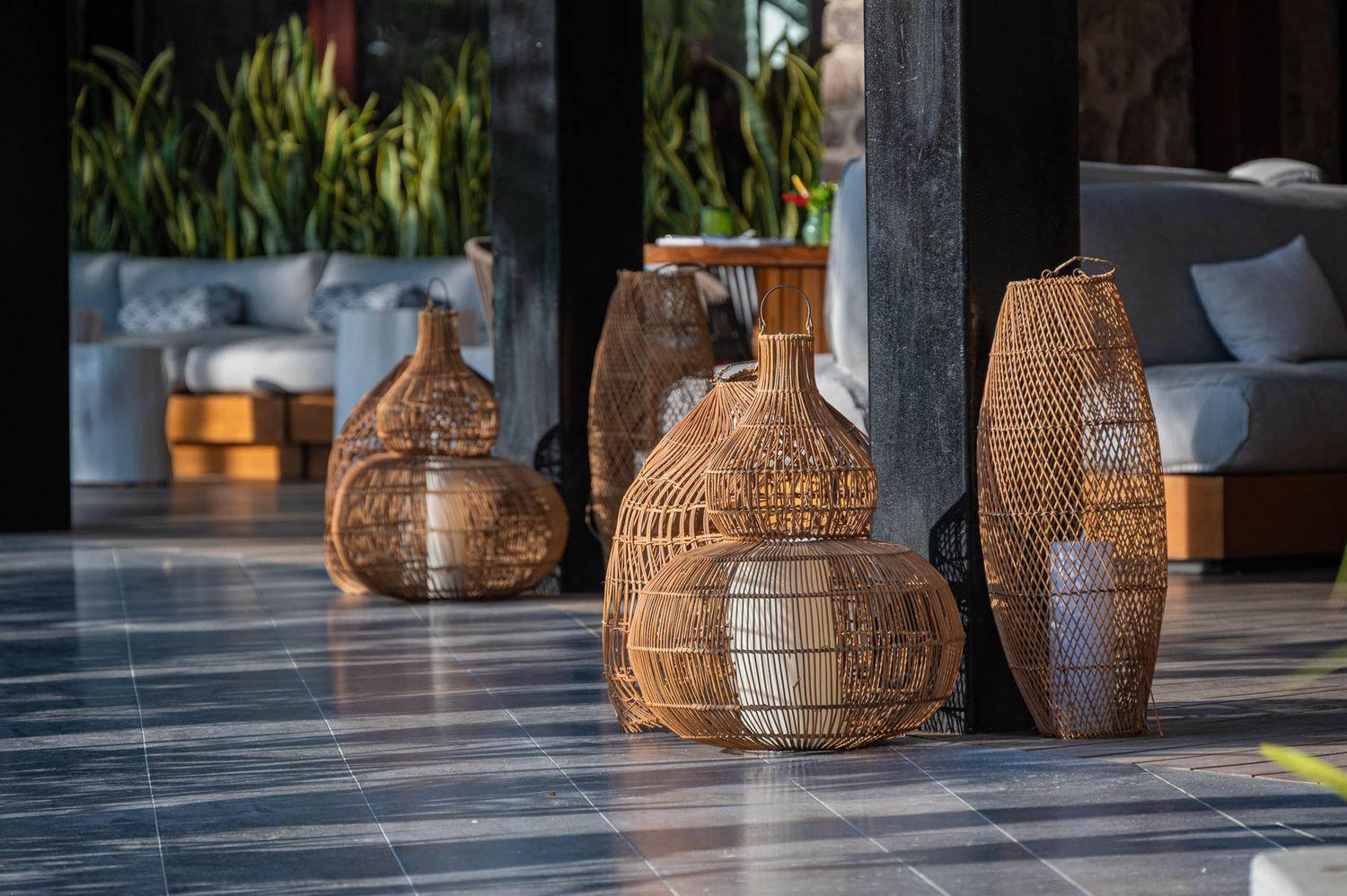 Decorative woven rattan lanterns and vases displayed on a marble floor in a tropical open-air lounge setting.
