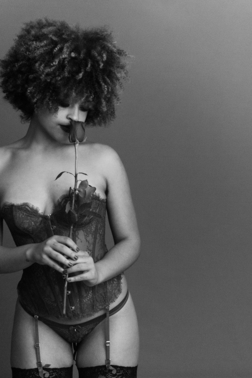 Artistic black and white photo of a woman in lace corset smelling a rose.
