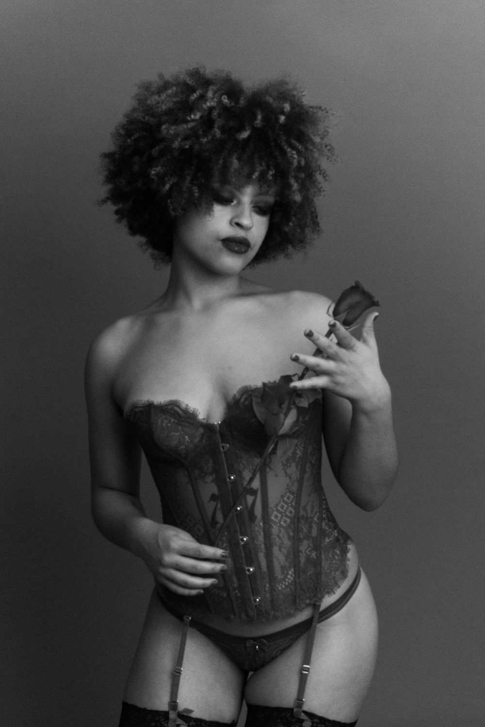 Monochrome photo of a curly-haired woman in lace corset and garter belt posing.