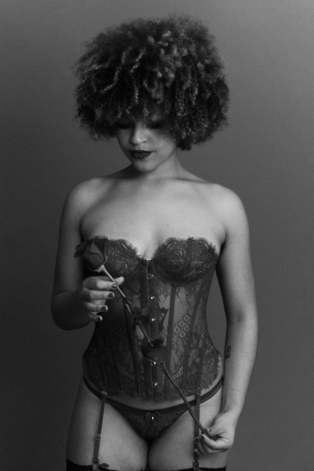Artistic monochrome image of a woman in lace corset and stockings holding a rose.