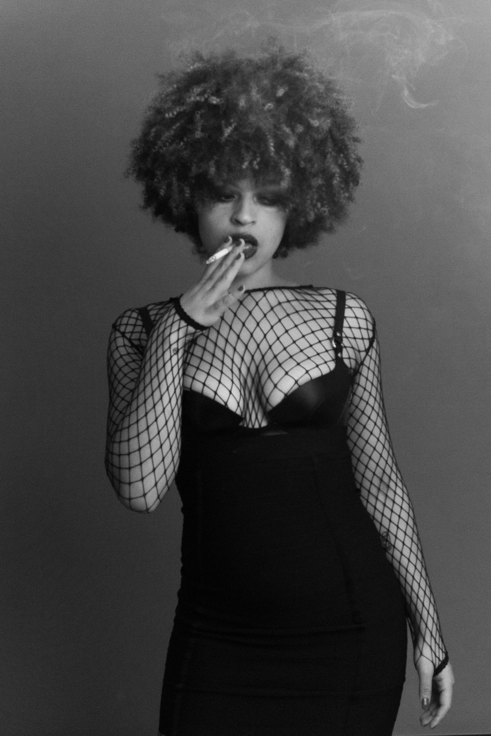 Black and white portrait of a woman in fishnet top and black dress smoking.