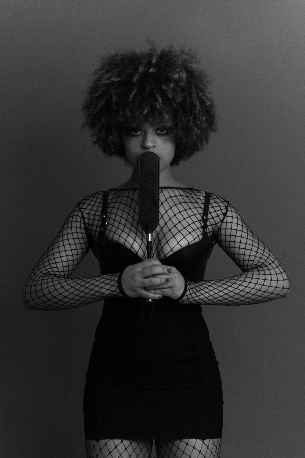 Black and white photo of a woman with afro hair in fishnet outfit holding a microphone close to her face.