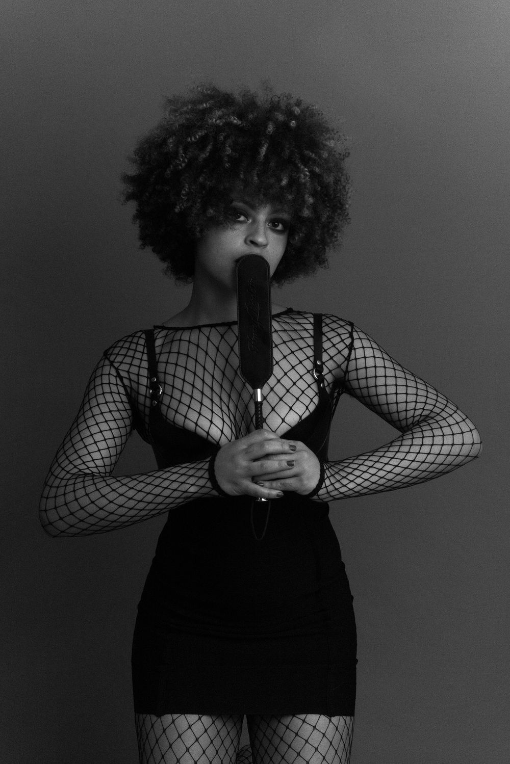 Black and white portrait of a woman with natural afro holding a microphone in a fishnet bodysuit.