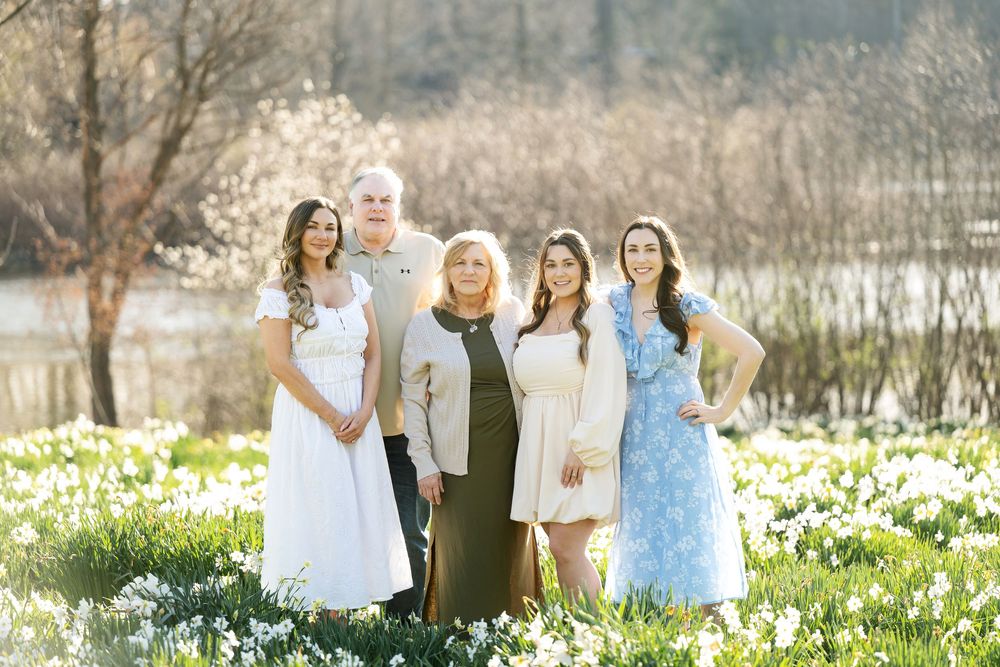 Five family members including an older couple and three young women posing in a sunny daffodil field.