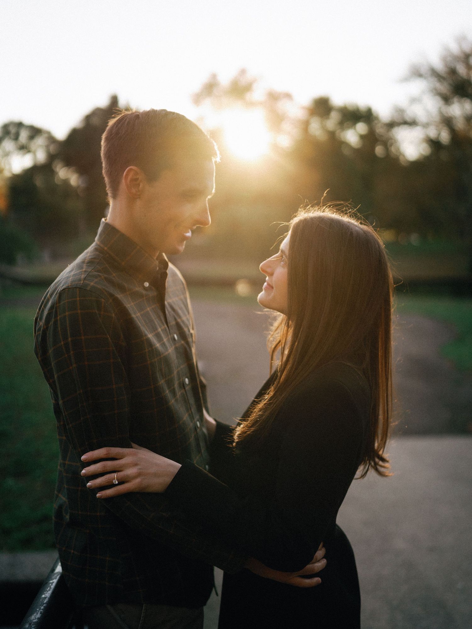 Couple embracing at golden hour sunset in a park, smiling at each other romantically.