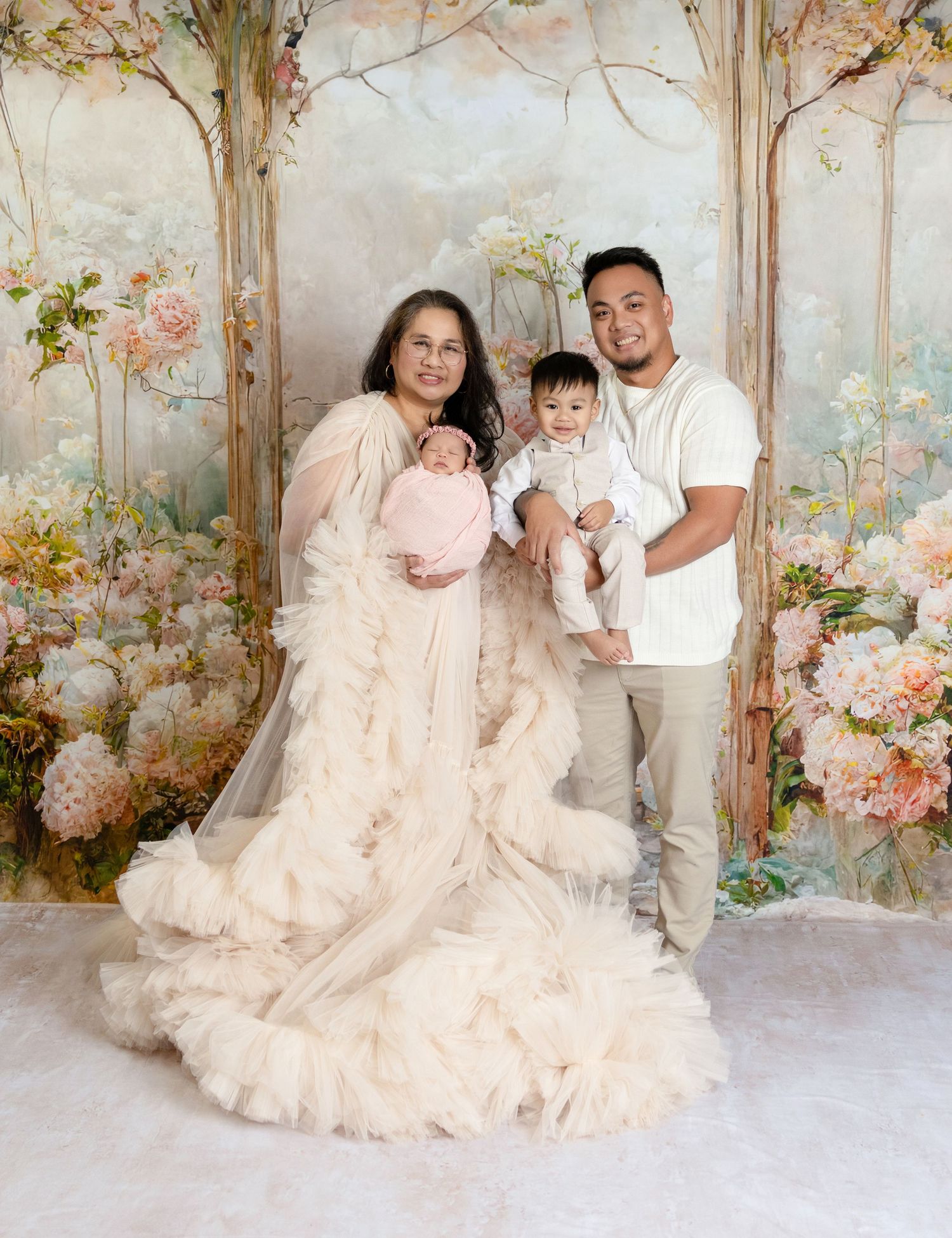 Parents in elegant attire pose with newborn and toddler before a romantic floral painted backdrop.