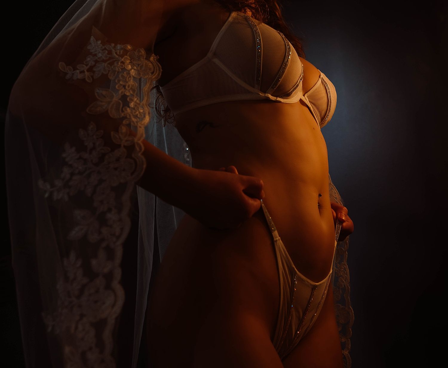 Woman in elegant white lace lingerie set posed against a dark moody background by Wisconsin boudoir photographer