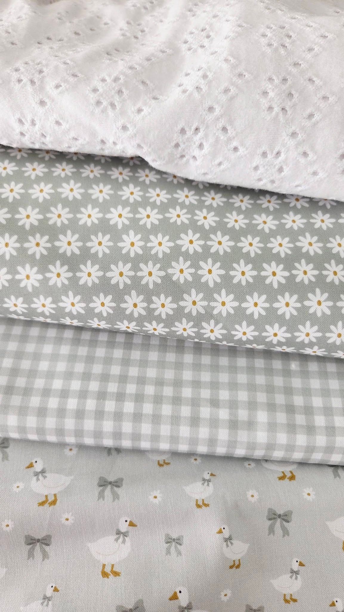 Four folded gray and white fabric swatches featuring eyelet lace, daisy print, gingham check, and duck with bow patterns.