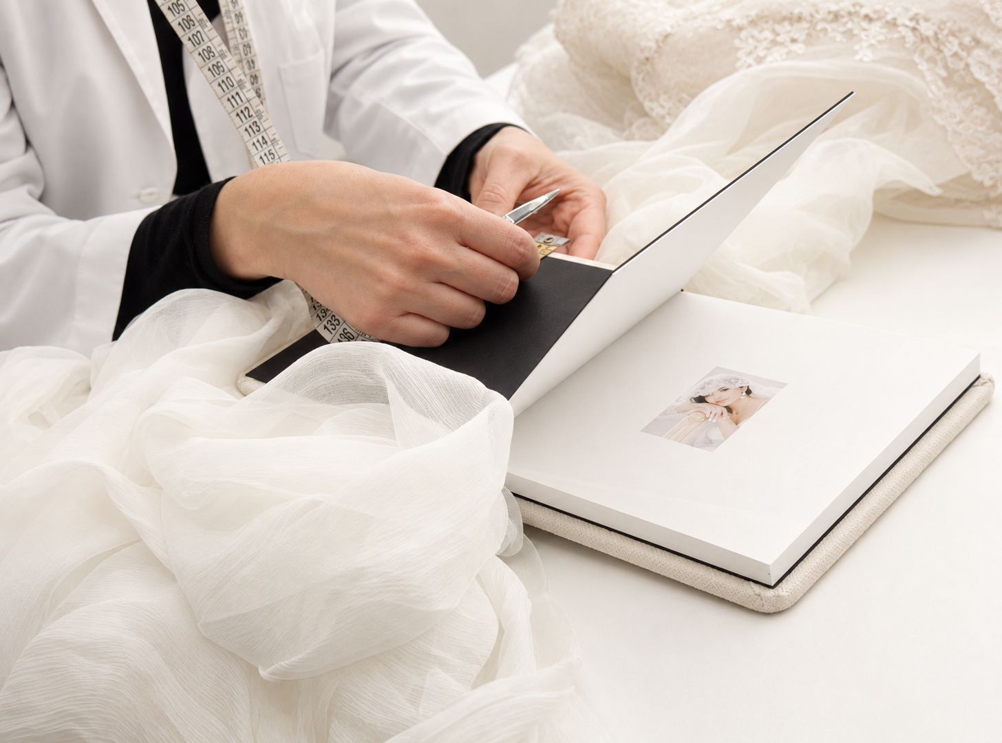 Bride reviewing a wedding photo album with elegant white fabric and a boxed photobook on a white table.