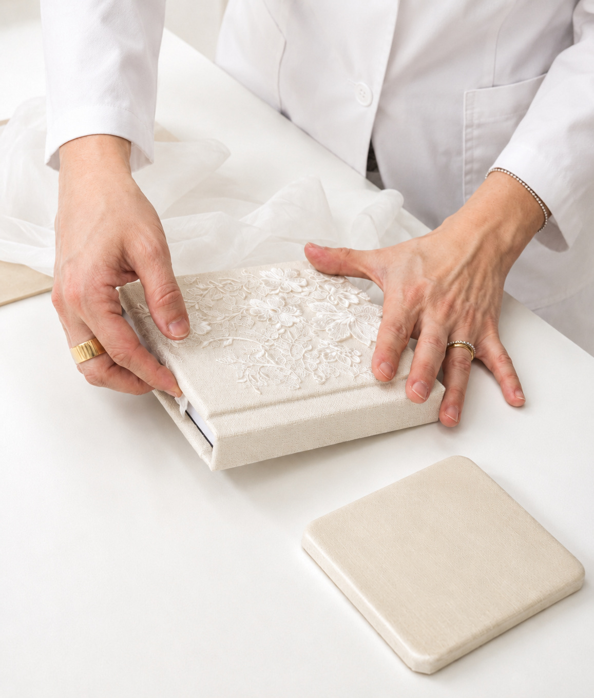 Person in white lab coat examining an ornate white textured box with tissue paper on a clean white surface.