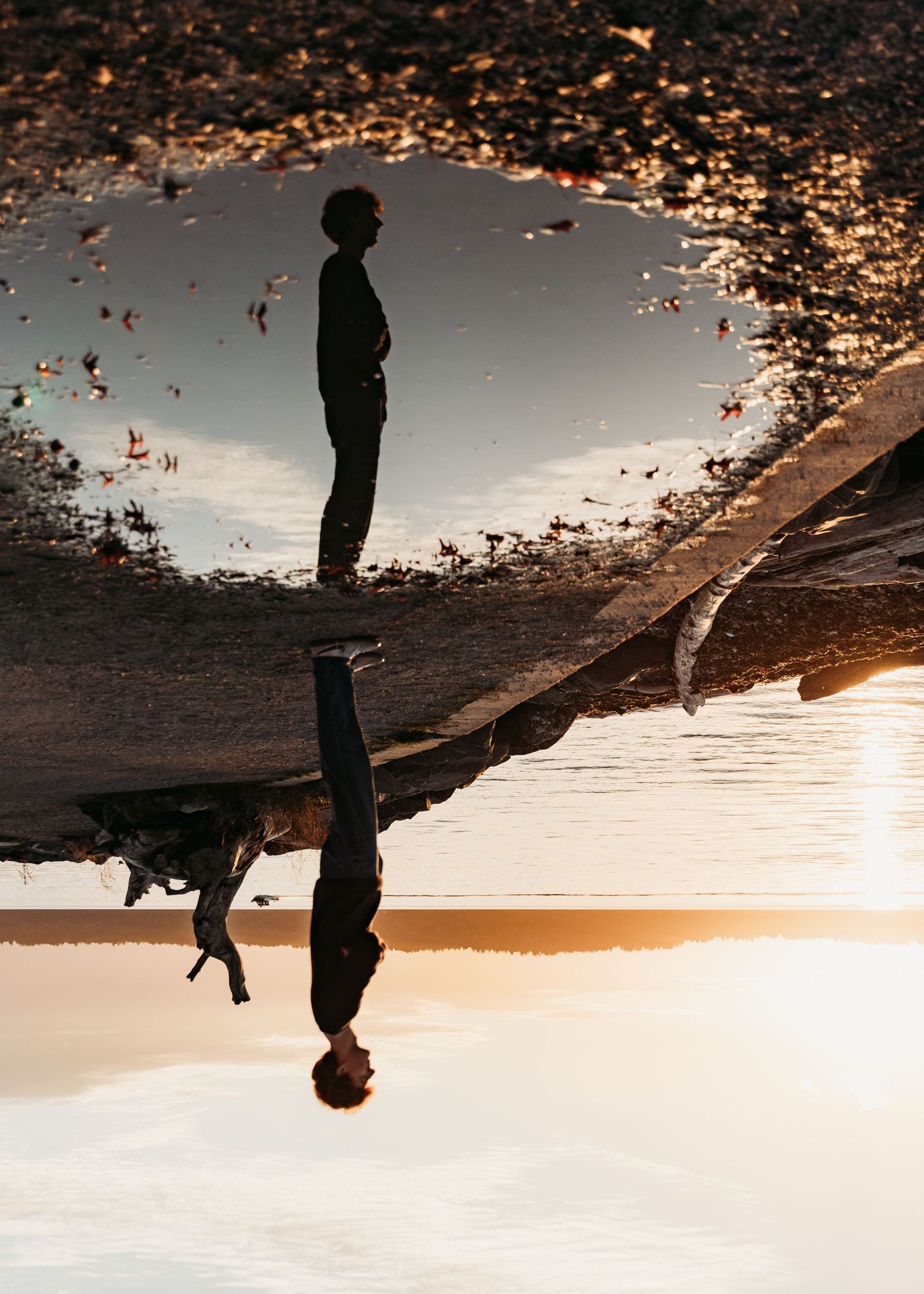 A person standing by a reflective puddle creates a stunning upside-down mirror image at golden hour.