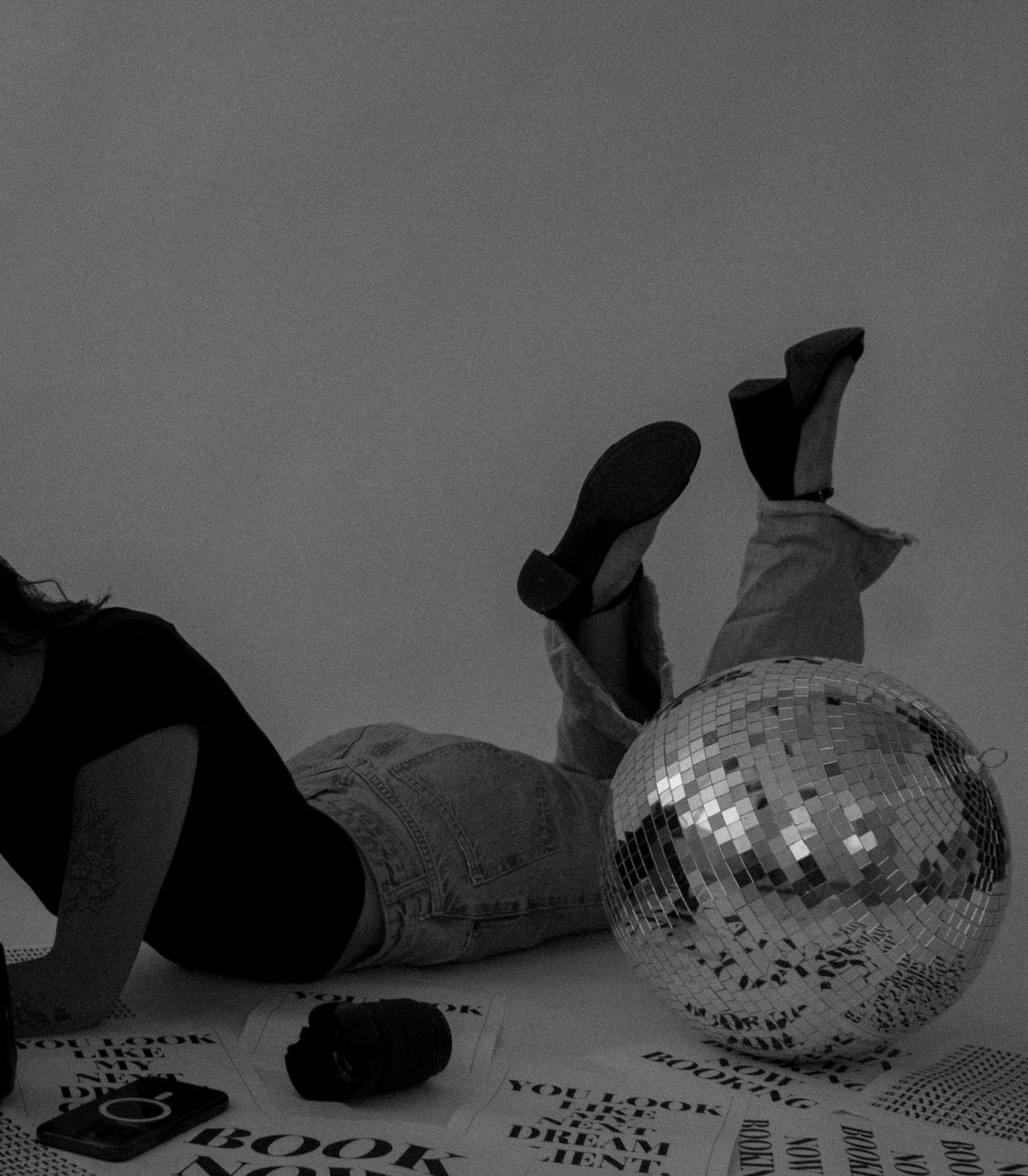 Black and white photo of person lying on floor with disco ball and scattered posters. Kingsport, TN