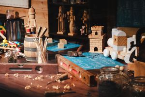 A wooden workbench cluttered with handcrafted wooden toys, tools, and wood shavings in a workshop.