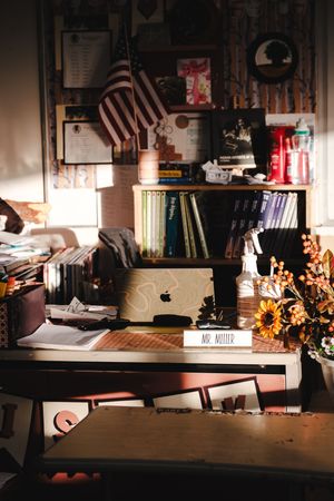 A warmly lit teacher's desk with an Apple laptop, sunflowers, and a nameplate reading Mr. Miller.