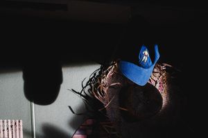A blue cowboy hat rests on a pile of colorful items in a dimly lit room with dramatic shadows.