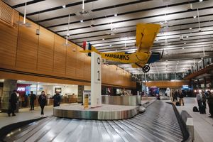 Fairbanks airport baggage claim with a vintage yellow plane suspended from the ceiling above the carousel.