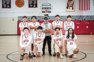 Youth basketball team poses for a group photo in a red and white gymnasium with their coach.