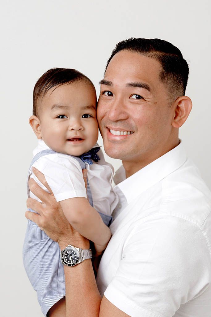 Proud dad smiles while holding his adorable baby boy for a studio portrait by professional French Valley baby photographer.