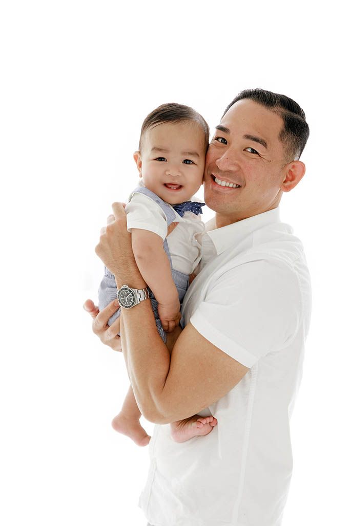 Smiling dad holds his happy baby boy in professional photography studio near French Valley California in Murrieta.