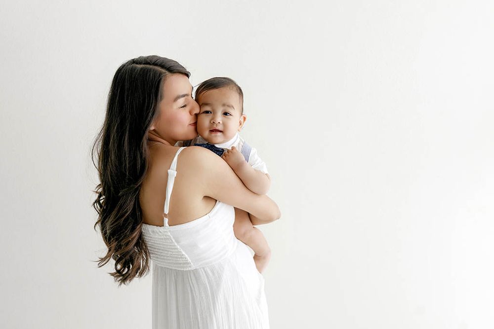 Mom kisses her baby boy against a clean white background by professional French Valley baby photographer.