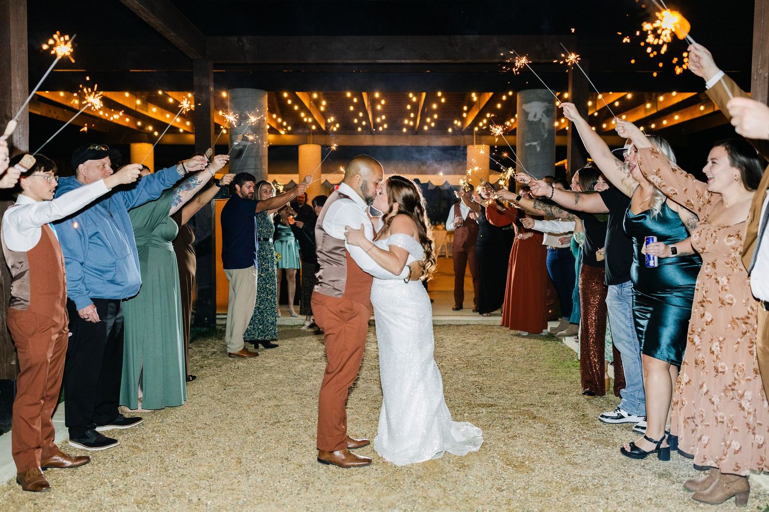 Bride and groom share a kiss during a sparkler send-off at an outdoor barn wedding reception at night.