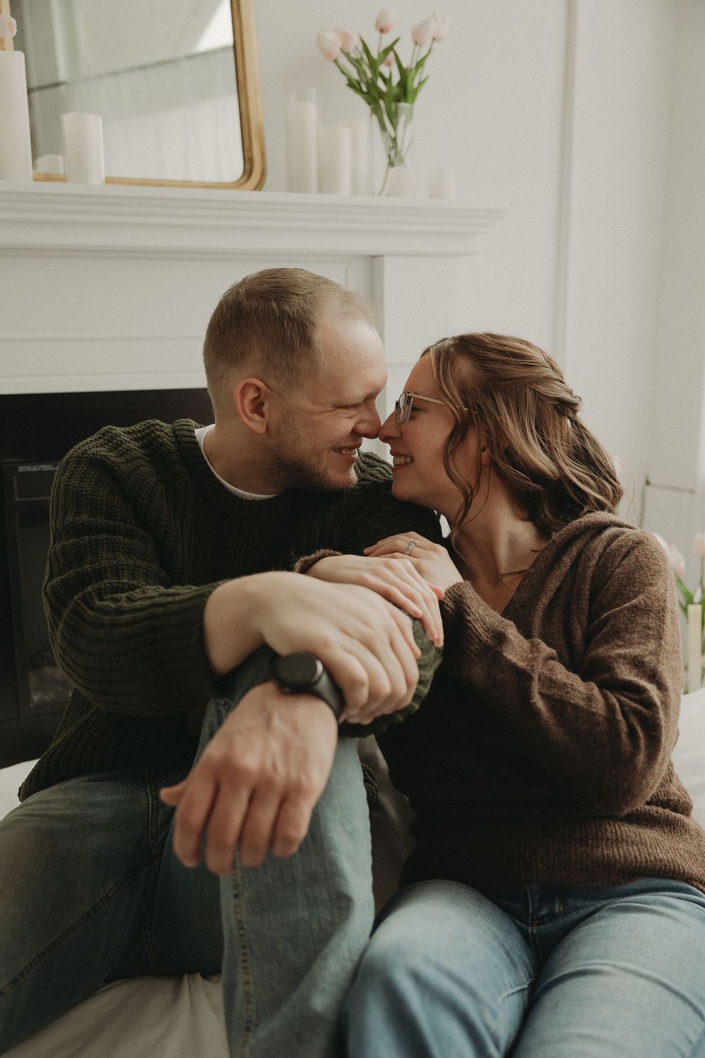 A couple shares a romantic moment by a fireplace, leaning in for a kiss in a cozy living room with tulips.