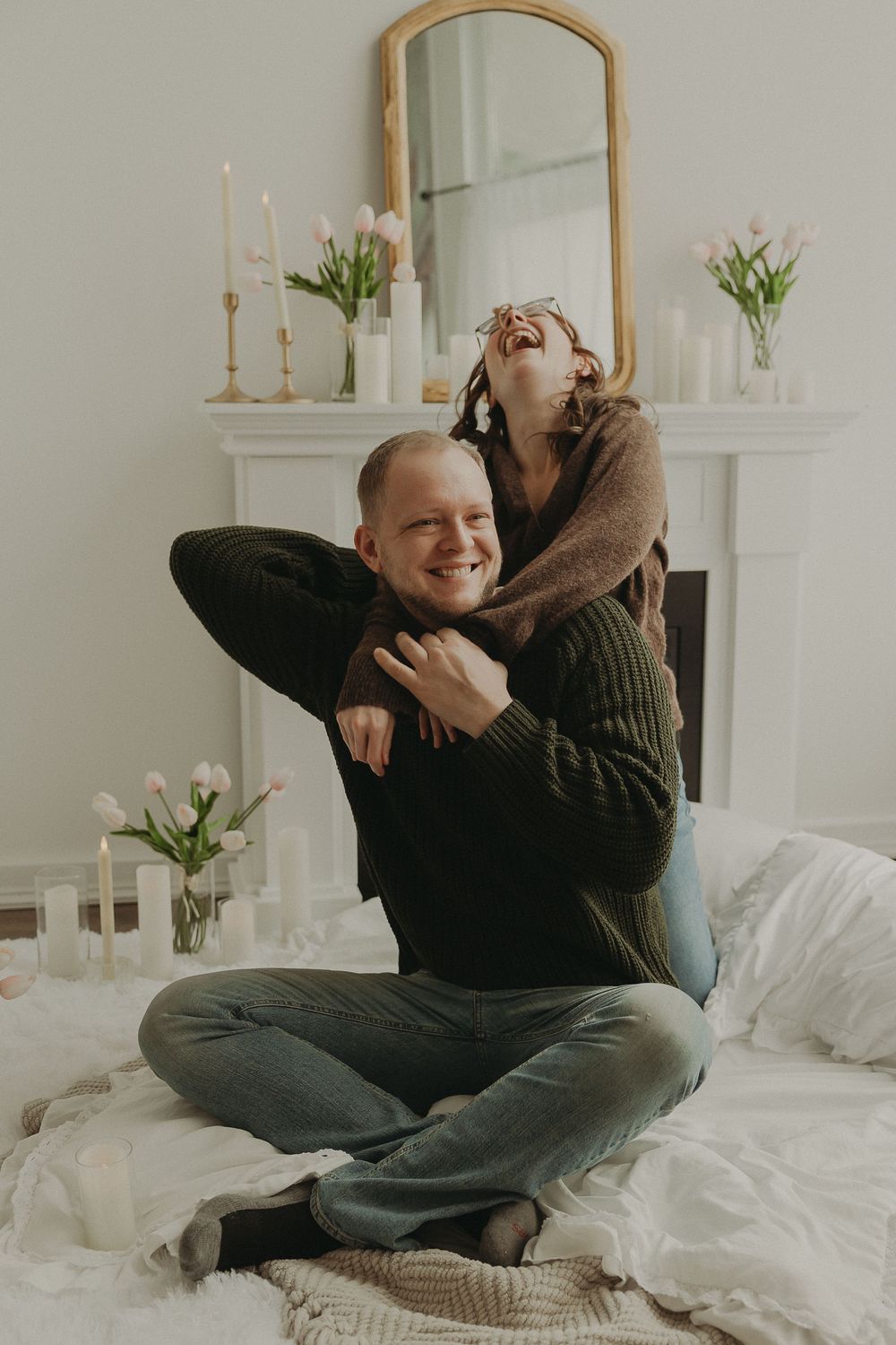 Happy couple embracing on a bed, laughing together in a romantic room with candles and tulips.