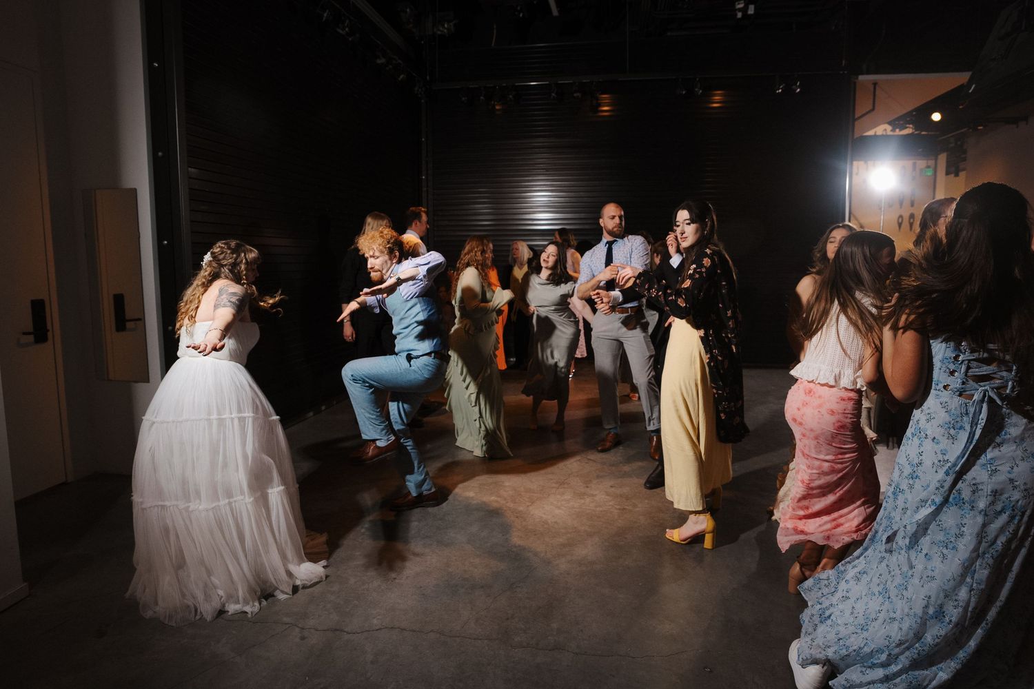 Wedding guests dancing joyfully at a reception venue, with bride in white gown visible among celebrating crowd.