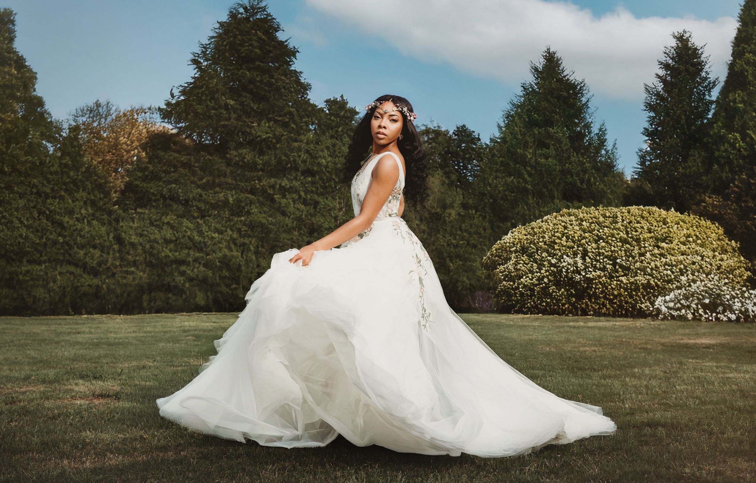 Bride in a flowing white ballgown twirling in a lush green garden on her wedding day.