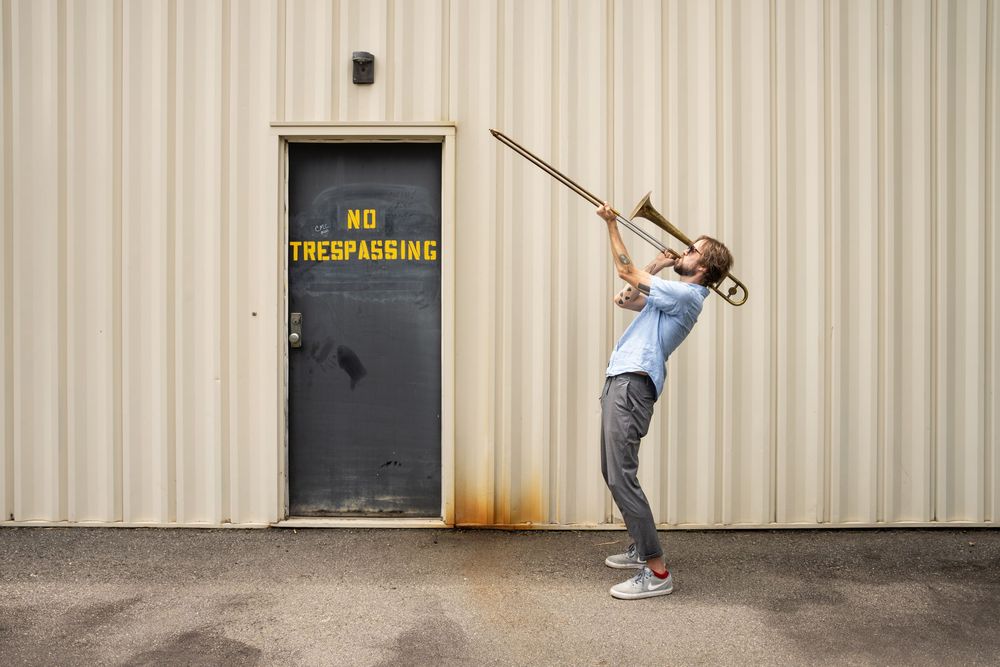 A person playing a long horn outside a industrial building; creative editorial and performance photography in Florence.