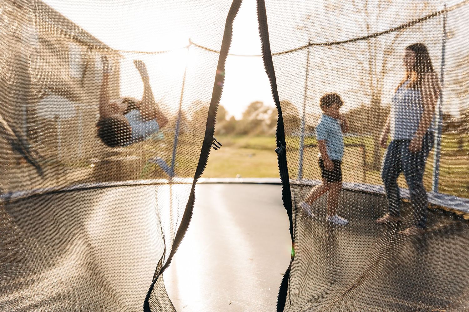 A family jumps and plays on a trampoline in their backyard.