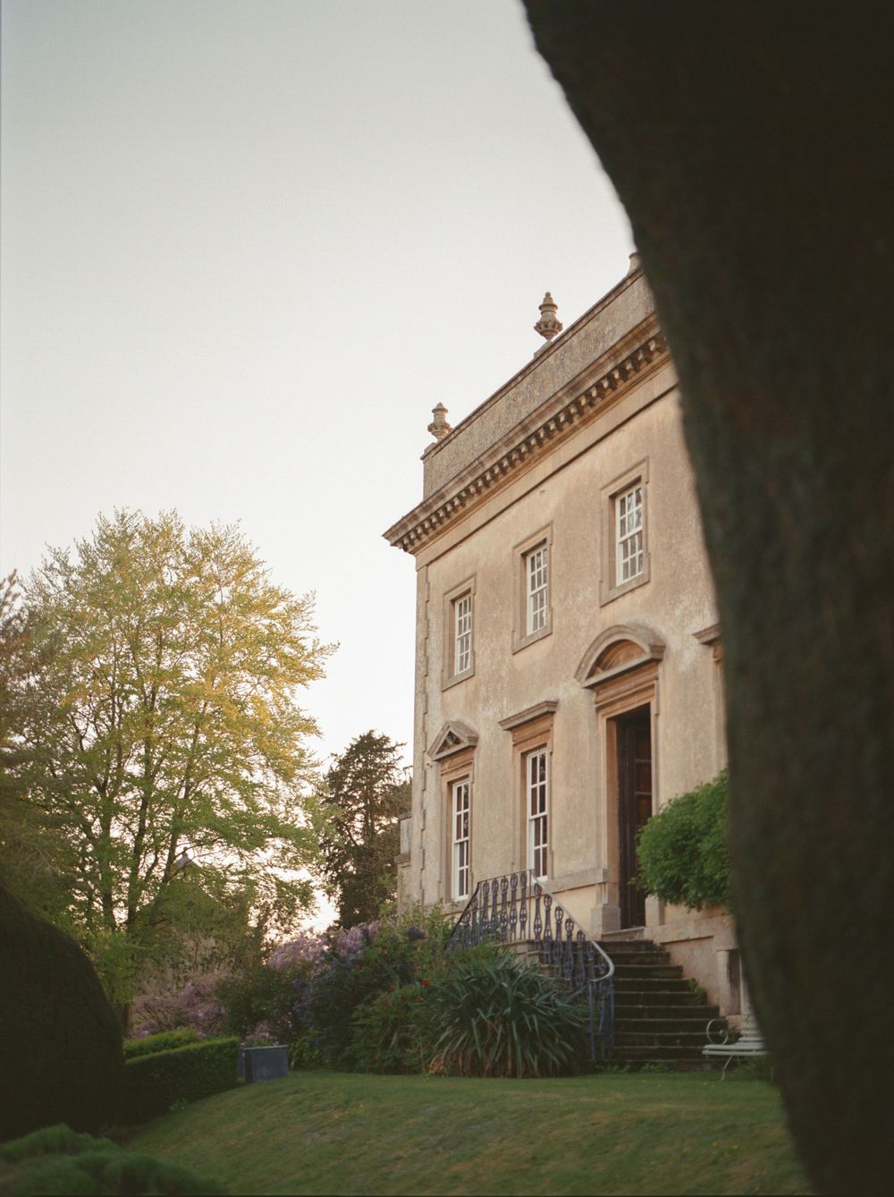 Georgian manor house with stone facade, arched doorway, and manicured gardens at dusk.