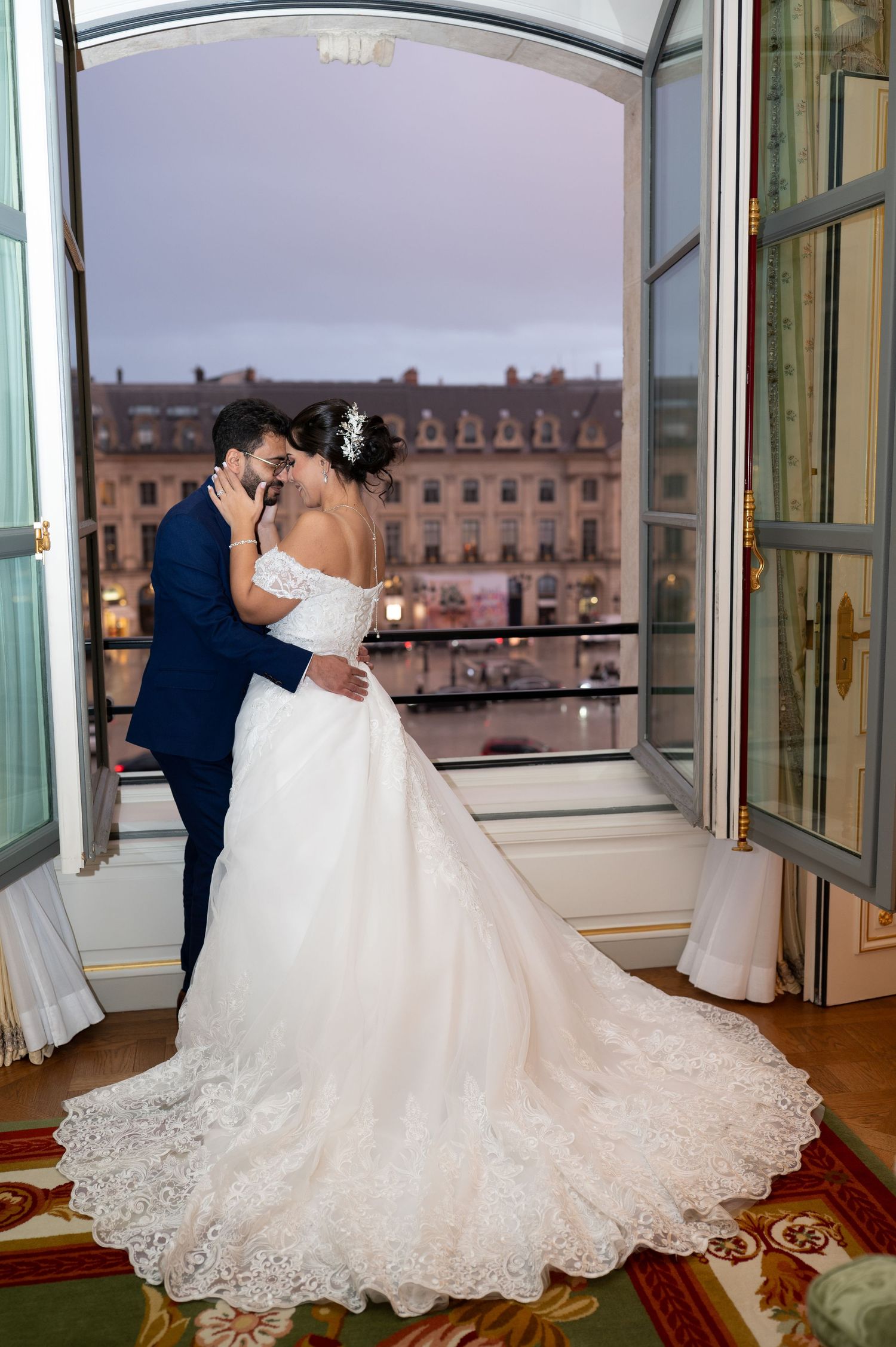 La mariée et le marié partagent une étreinte romantique sur le balcon d'un hôtel parisien, avec des lumières de la ville qui brillent au cré