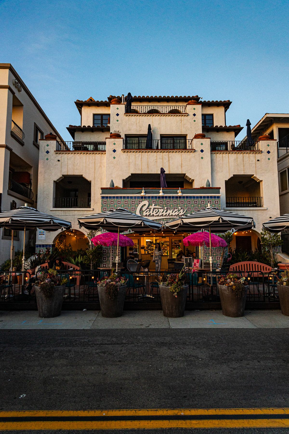 Caterina's restaurant exterior with Spanish Colonial architecture, pink umbrellas, and outdoor dining at dusk in California.