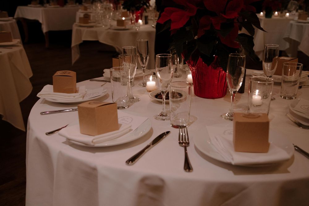 Elegant wedding reception table setting with white linens, candles, wine glasses, and gold favor boxes.