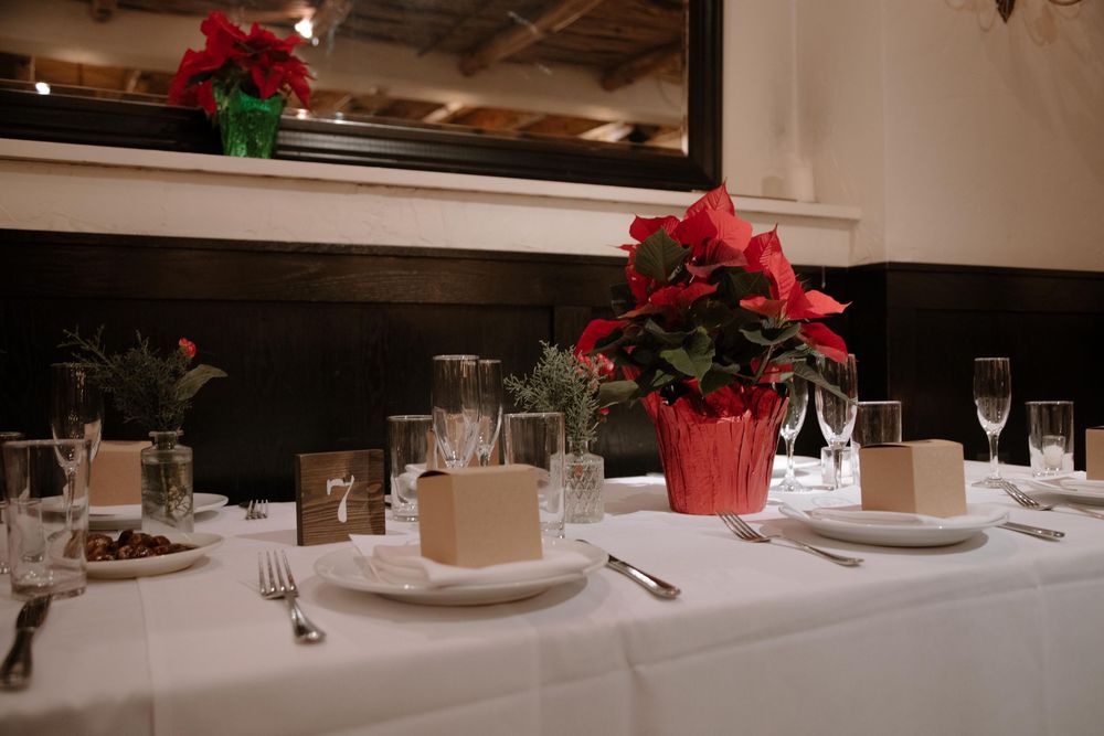 Elegant Christmas table setting with red poinsettia centerpiece, white tablecloth, place cards, and glassware in a restaurant.