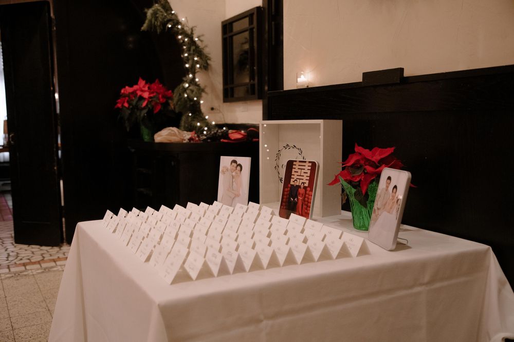 Wedding seating chart display table with white place cards, framed artwork, and poinsettias near a decorated Christmas tree.