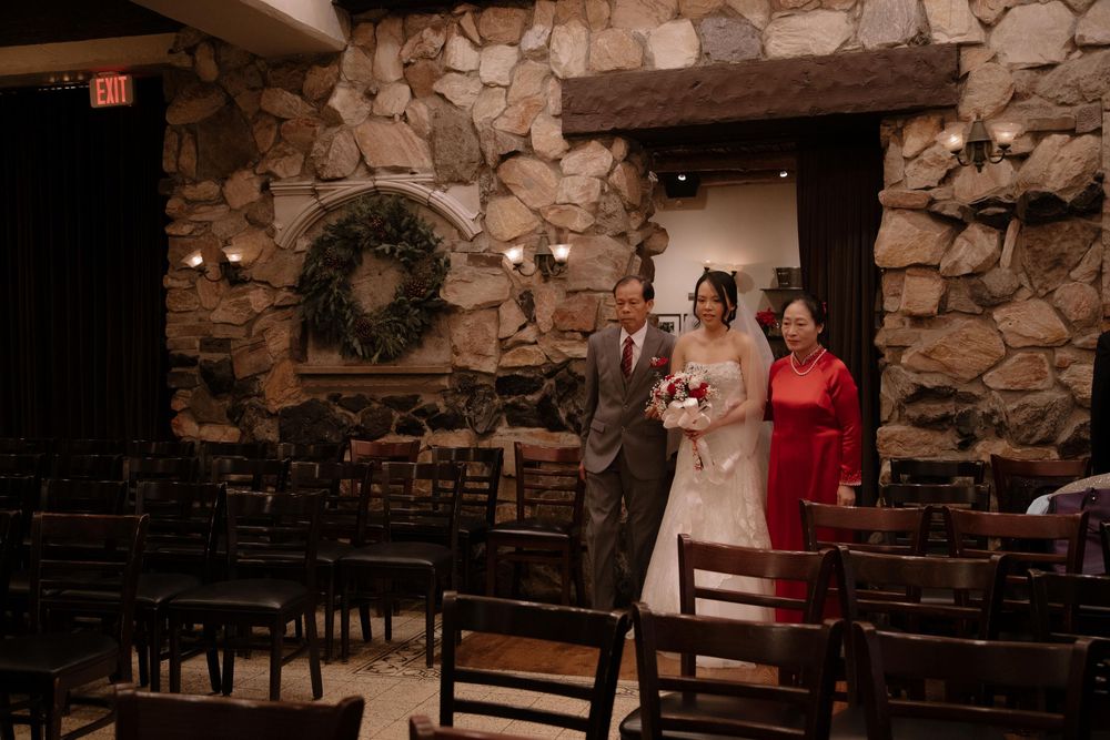 Bride walks down the aisle with family in a rustic stone chapel decorated with a wreath for a winter wedding.