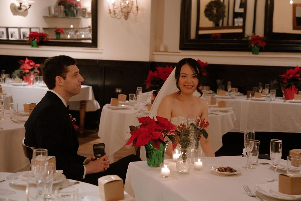 Bride and groom smiling at wedding reception table adorned with red poinsettias and candles in festive restaurant.