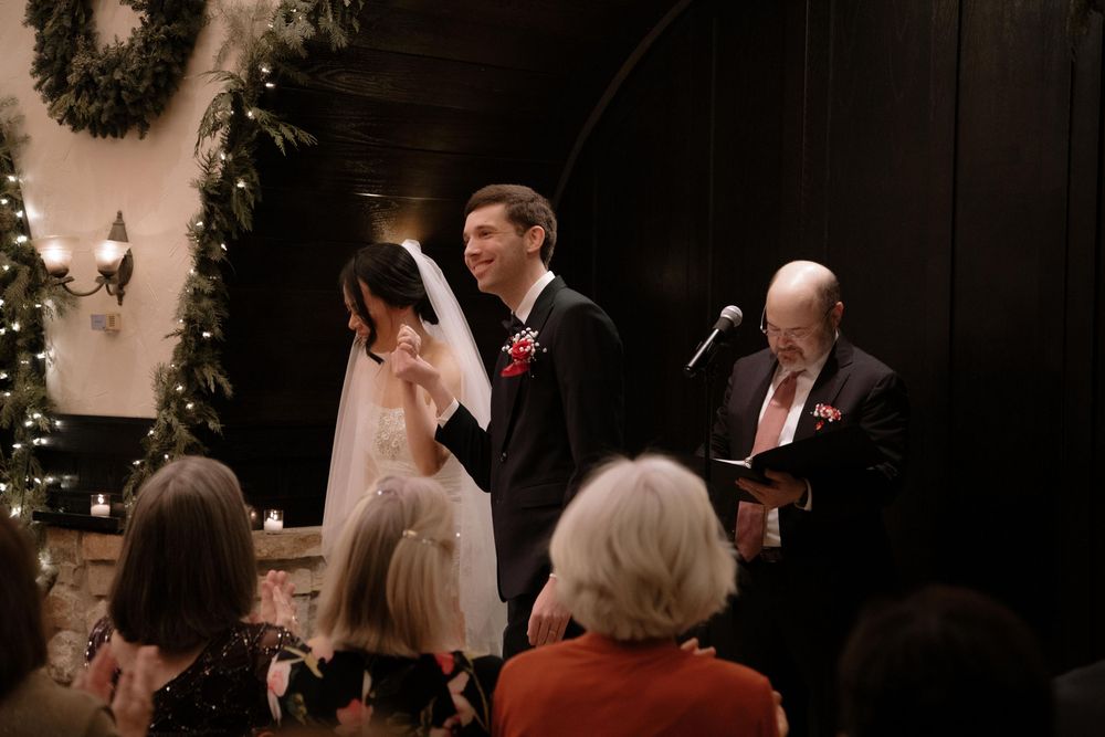 Bride and groom exchange vows at elegant winter wedding ceremony with festive greenery decorations.