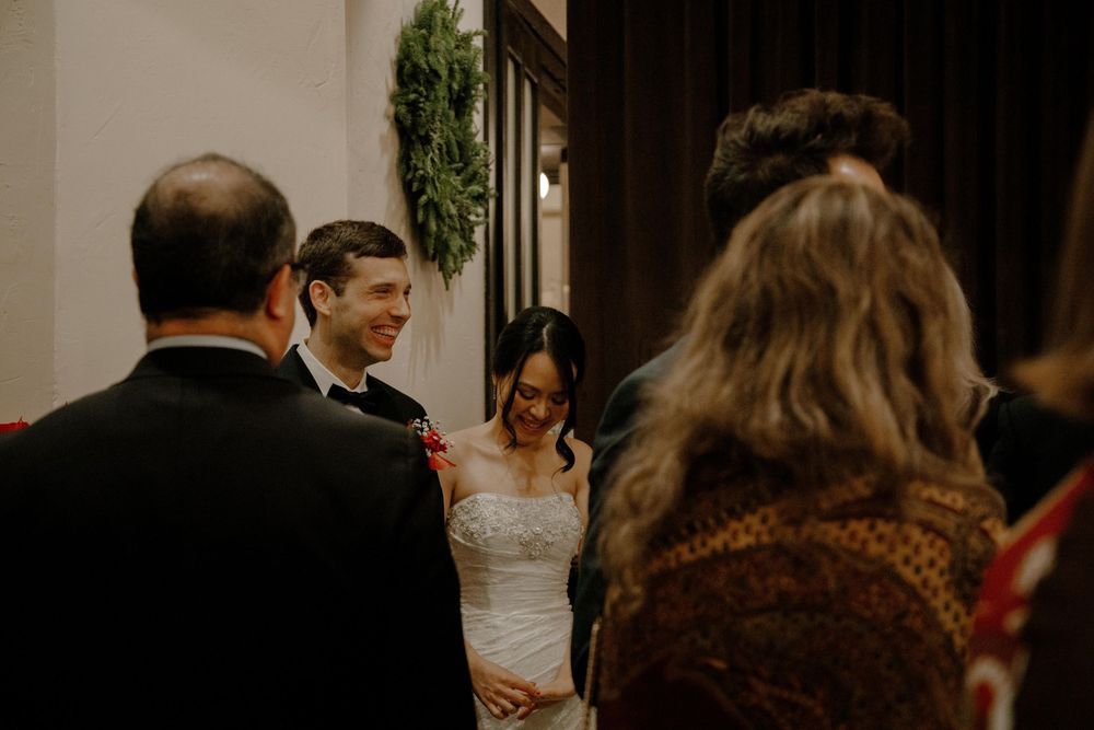 Smiling bride and groom stand together during wedding ceremony greeting guests in an elegant indoor venue.