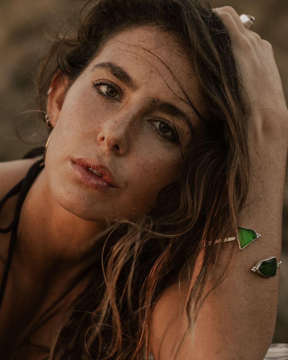 Woman with freckles and wavy hair wearing green gemstone jewelry, posing outdoors in natural light.