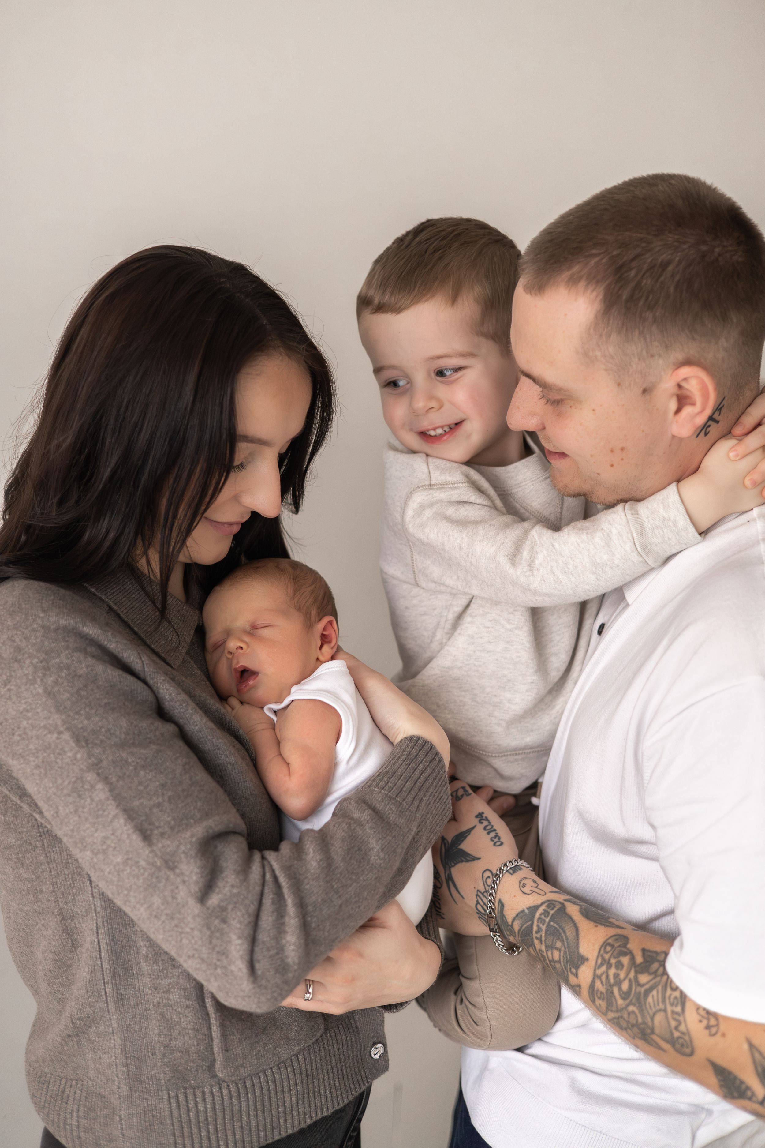 A young family with holds their newborn baby as their smiling toddler hugs dad in a warm portrait baby photographer Nottingham newborn
