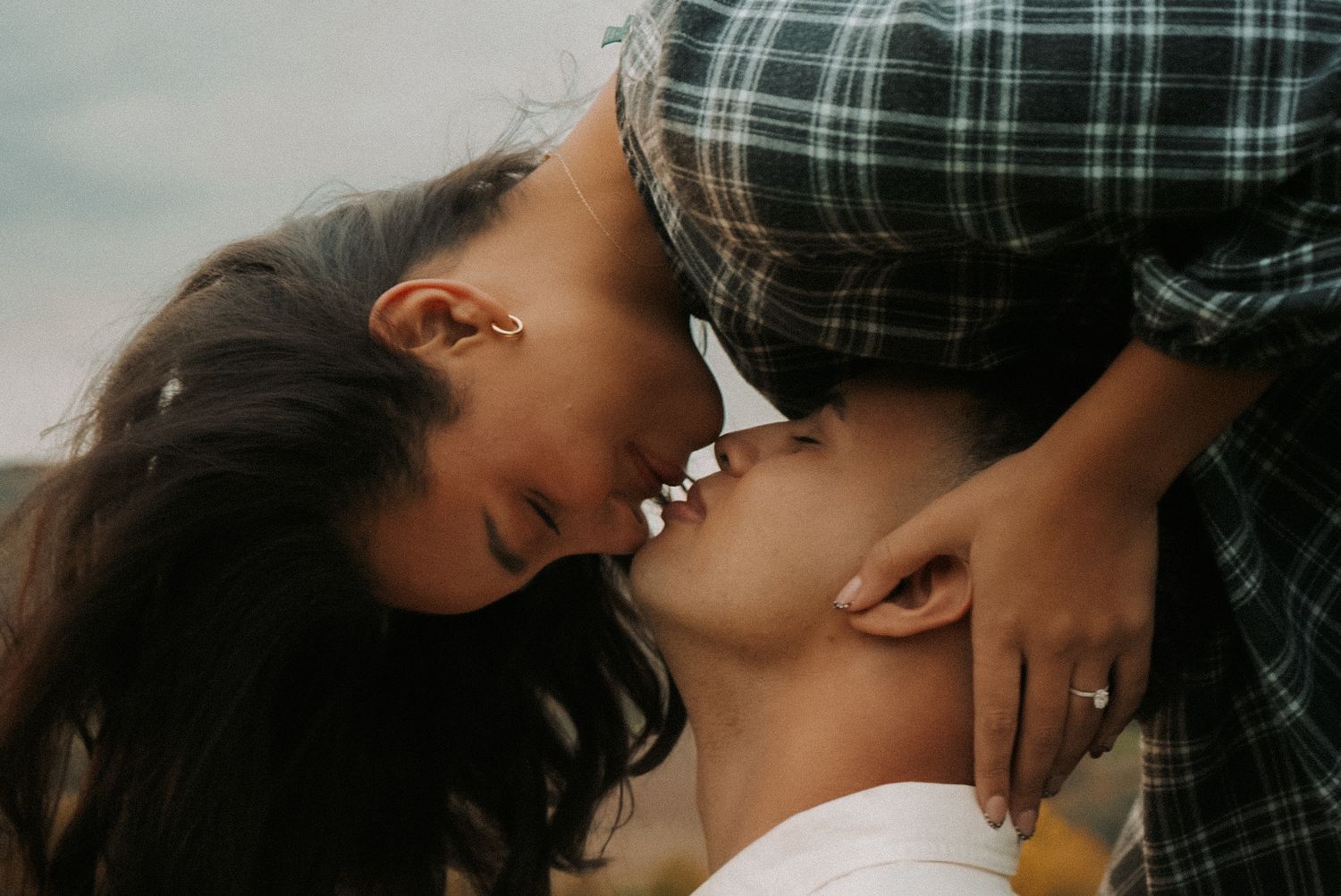 A couple shares an intimate upside-down kiss outdoors with a dramatic cloudy sky above them, beautiful German countryside behind them.