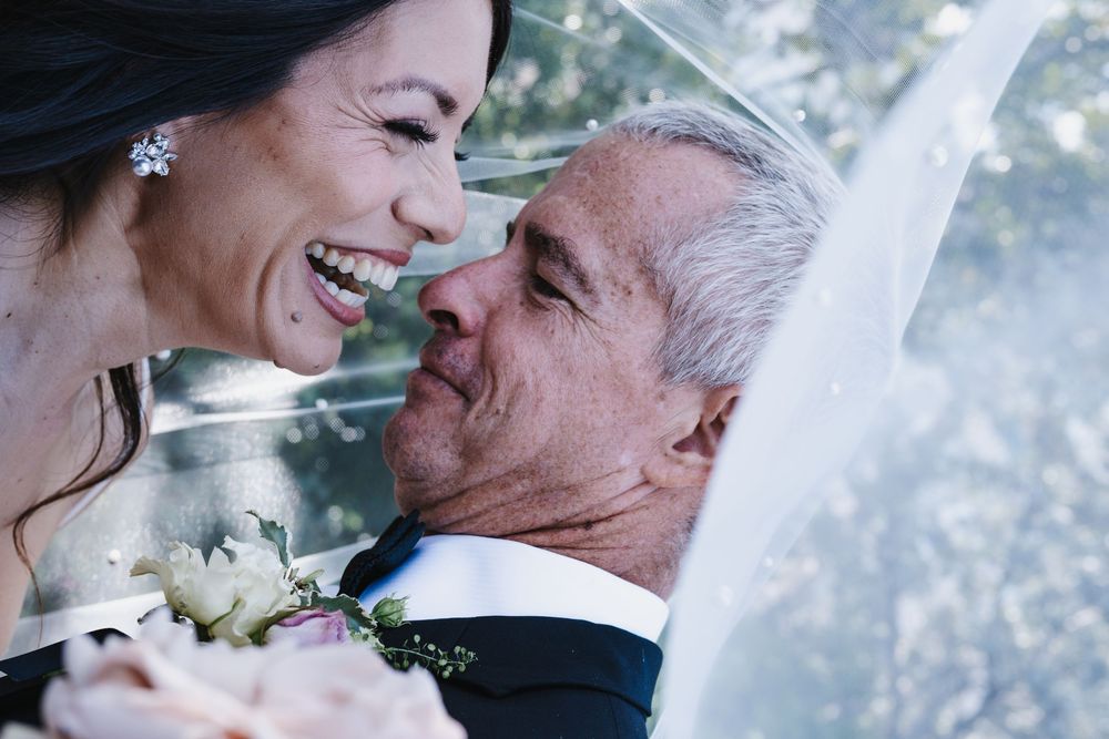 Happy bride and groom share a romantic moment under a veil, smiling closely together on their wedding day.