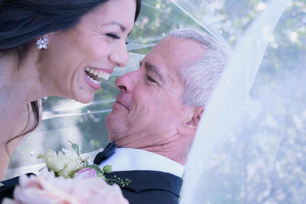 Happy couple sharing a romantic moment under a veil on their wedding day, bride holding a bouquet.