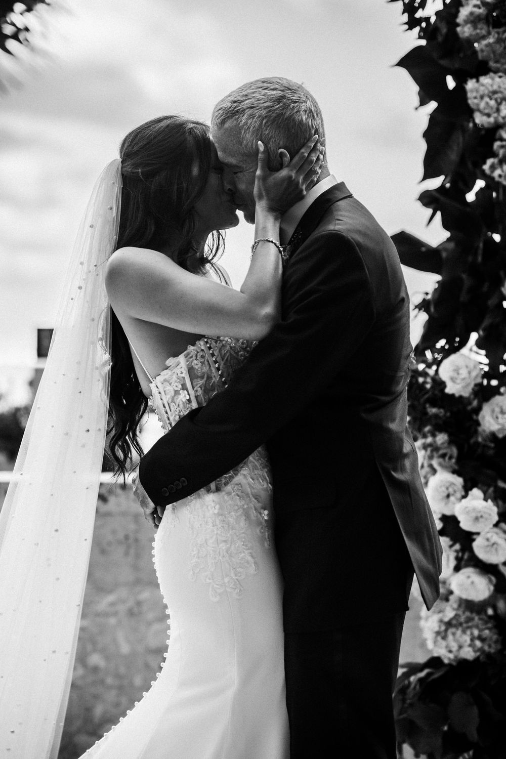 Black and white photo of a bride and groom sharing their first kiss at an outdoor wedding ceremony.