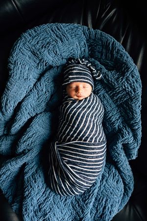A series of newborn photos showing a baby wrapped in navy blue textured blanket wearing a striped hat.