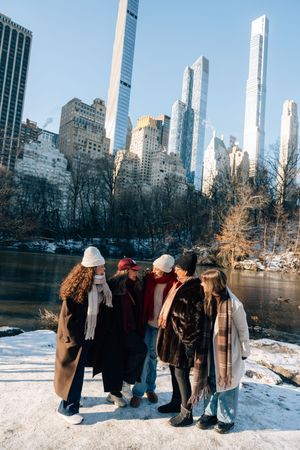 A group of people bundled in winter coats stand in snowy Central Park with Manhattan skyscrapers towering in the background.
