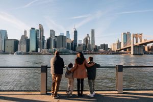 Three people standing at the waterfront overlooking the Manhattan skyline and Brooklyn Bridge in New York City.